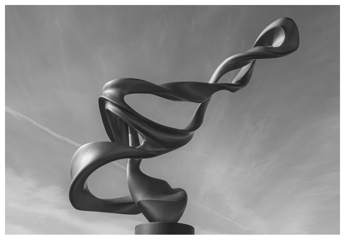 A black and white photograph of Nuance, a metal sculpture by Don Frost, with a contrail in the sky in the background.