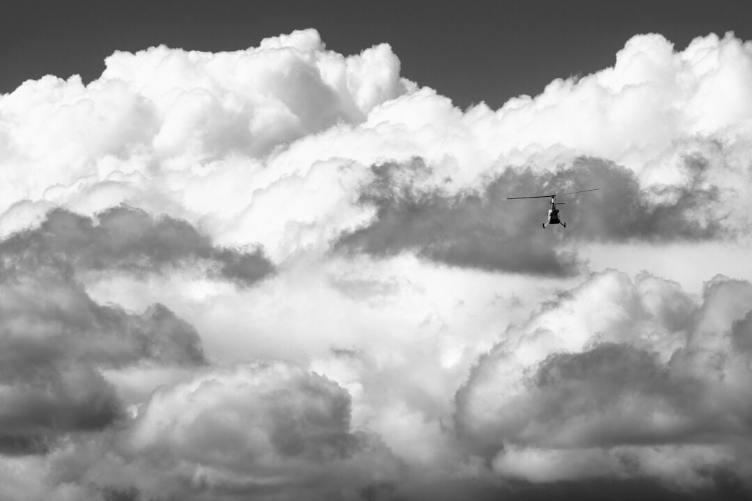 A helicopter small against a wall of clouds