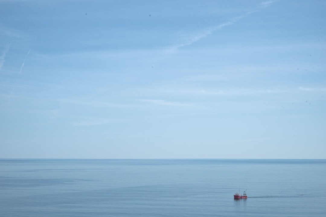 A small fishing boat in a large, calm blue sea against a blue sky streaked with clouds